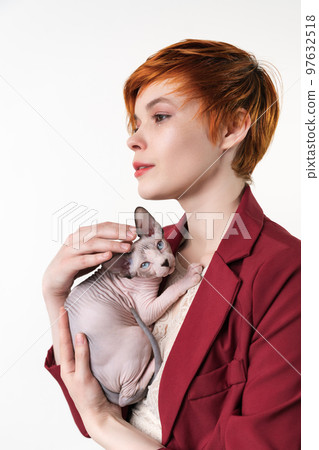 Hipster young redhead woman with short hair gently hugging to her chest Sphynx Hairless Cat. Beautiful woman looking away, dressed in red jacket. Studio shot on white background. Part of series. 97632518
