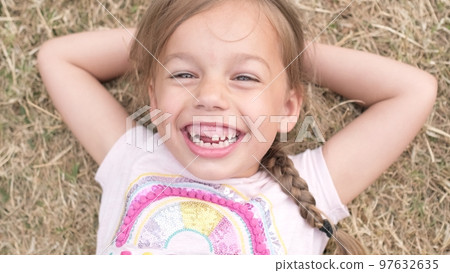 Little Happy toothless and Smiling Child Girl Laying on Yellow Lawn Dry Grass Hay in Park. Summer Time, Nature, Dreams, Lifestyle Country life farm village. Smilling Face Close up Looking at Camera 97632635