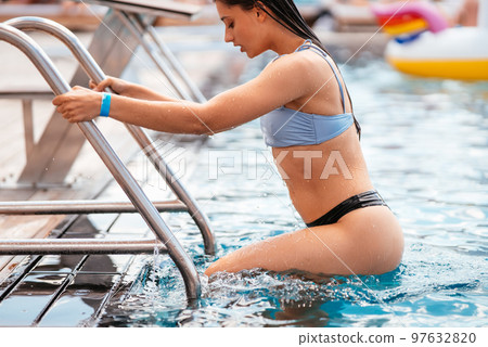 Young woman climbs the ladder out swimming pool Young woman climbs the ladder out swimming pool 97632820