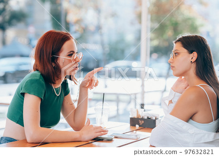 Two pretty girlfriends talking while sitting in a bar outdoors Two pretty girlfriends talking while sitting in a bar outdoors 97632821