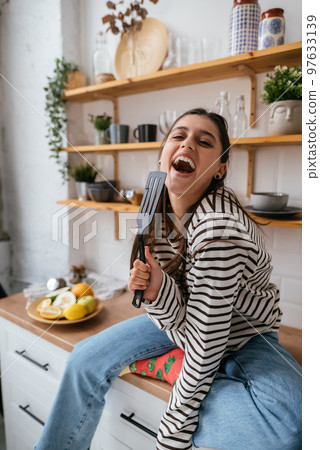 Funny woman singing into spatula, holding spatula as microphone. Funny woman singing into spatula, holding spatula as microphone. 97633139