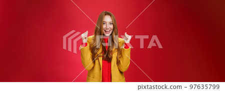 Hooray success. Portrait of happy cheerful and sincere cute ginger woman in yellow coat raising clenched fists and celebrating joyfully positive news, triumphing over win and smiling broadly Hooray success. Portrait of happy cheerful and sincere cute ginger woman in yellow coat raising clenched fists and celebrating joyfully positive news, triumphing over win and smiling broadly 97635799