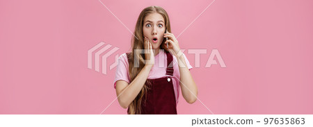 Waist-up shot of shocked woman learning stunning news via smartphone talking on phone holding cellphone near ears folding lips and gasping in surprise popping eyes at camera worried over pink wall Waist-up shot of shocked woman learning stunning news via smartphone talking on phone holding cellphone near ears folding lips and gasping in surprise popping eyes at camera worried over pink wall 97635863