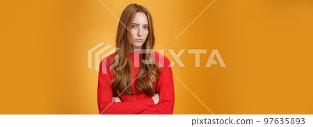 Suspicious intense and defensive ginger girl standing in passive-aggressive pose pouting and frowning looking with disbelief and disdain at camera, offended against orange background Suspicious intense and defensive ginger girl standing in passive-aggressive pose pouting and frowning looking with disbelief and disdain at camera, offended against orange background 97635893