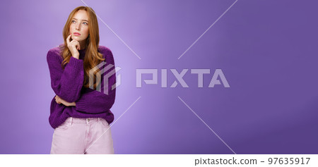 Thoughtful and focused smart, creative attractive woman with red hair and freckles squinting, looking at upper left corner while thinking having idea or plan holding hand on chin as making up choice 97635917