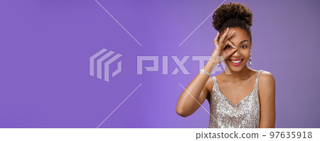 Elegant lucky confident feminine african-american woman in silver fashionable dress show okay ok gesture on eye peeking forward gladly smiling self-assured like perfection, stand blue background 97635918