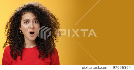 Confused and frustrated young questioned woman with curly hair open mouth and raising eyebrow in surprise being displeased with unfair situation standing clueless and upset over yellow background 97636594