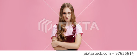 I mad on world. Unhappy hateful young arrogant girl in overalls with wavy natural hairstyle crossing arms against chest in defensive pose lifting upper lip in scorn and disdain, looking with anger 97636614