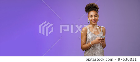 Attractive stylish confident african-american woman in silver shiny dress holding smartphone messaging scrolling internet gadget looking lucky happily camera standing blue background rejoicing Attractive stylish confident african-american woman in silver shiny dress holding smartphone messaging scrolling internet gadget looking lucky happily camera standing blue background rejoicing 97636811