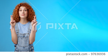 Hopeful relaxed optimistic cute european redhead curly girl smiling faithfully awaiting good results believe wish come true cross fingers good luck grin anticipating important news dream fulfill 97636936