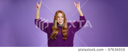 Girl feeling excited finally receiving tickets for favorite band show, raising hands with rock-n-roll gesture yelling yeah and smiling broadly, happy and thrilled against purple background 97636938