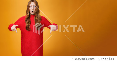 Wow what awesome promotion. Portrait of impressed and surprised cute wondered redhead woman in stylish warm knitted dress folding lips in amazement pointing down and looking at camera Wow what awesome promotion. Portrait of impressed and surprised cute wondered redhead woman in stylish warm knitted dress folding lips in amazement pointing down and looking at camera 97637133