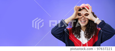Girl see us as imitating peek with binocular making circles over eyes and looking through it joyful and excited, having fun fooling around posing happy and cute over blue background in outdoor outfit Girl see us as imitating peek with binocular making circles over eyes and looking through it joyful and excited, having fun fooling around posing happy and cute over blue background in outdoor outfit 97637221