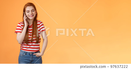 Friendly talkative good-looking redhead female chatting lively discuss ordinary things hold smartphone near ear, close eyes smiling joyfuly, communicating, listen voice message, orange background 97637222