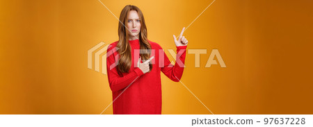 Intense suspicious and doubtful european ginger girl in warm sweater frowning hesitant and confused pointing at upper left corner asking question, looking with disbelief over orange background Intense suspicious and doubtful european ginger girl in warm sweater frowning hesitant and confused pointing at upper left corner asking question, looking with disbelief over orange background 97637228