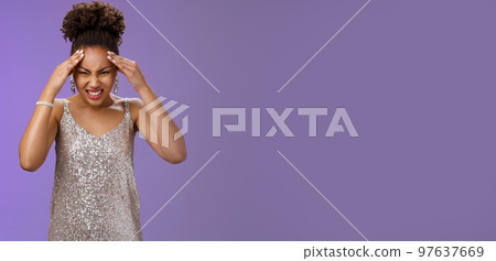 Pressured intense worried african-american woman in silver glittering dress grimacing cringing painful headache hold hand forehead suffer pain migraine, standing bothered blue background Pressured intense worried african-american woman in silver glittering dress grimacing cringing painful headache hold hand forehead suffer pain migraine, standing bothered blue background 97637669