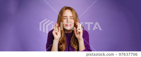 Hopeful and dreamy cute tender redhead 20s girl in purple sweater making wish faithfully close eyes and cross fingers for good luck as anticipating miracle happen, supplicating over violet wall Hopeful and dreamy cute tender redhead 20s girl in purple sweater making wish faithfully close eyes and cross fingers for good luck as anticipating miracle happen, supplicating over violet wall 97637706