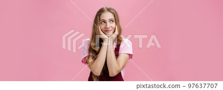 Girl wonders if she have sweets in fridge. Portrait of charming dreamy young woman in trendy outfit leaning head on palms gazing at upper left corner with tender smile daydreaming, feeling nostalgic Girl wonders if she have sweets in fridge. Portrait of charming dreamy young woman in trendy outfit leaning head on palms gazing at upper left corner with tender smile daydreaming, feeling nostalgic 97637707