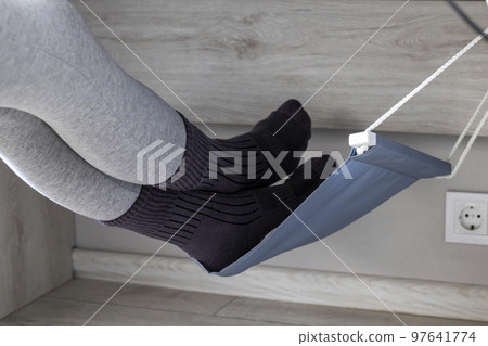 The woman's legs are lying in a leg hammock under the table. Vein health care for varicose veins. The woman's legs are lying in a leg hammock under the table. Vein health care for varicose veins. 97641774
