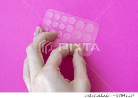 Woman tears off an acne patch to stick on her skin. Acne patches on a pink background View from above. 97642154