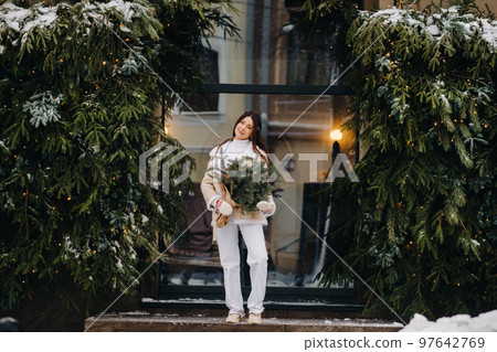 A girl with long hair in winter on the street with a bouquet of fresh fir branches 97642769
