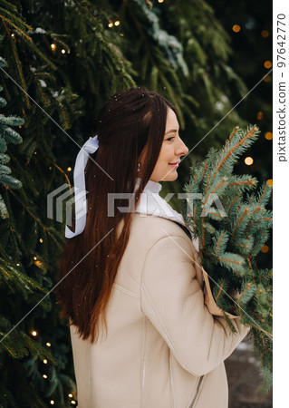 A girl with long hair stands with her back in a winter forest with a bouquet of fir branches. Snowy winter 97642770