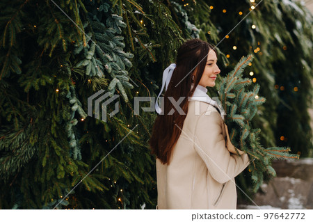 A girl with long hair stands with her back in a winter forest with a bouquet of fir branches. Snowy winter 97642772