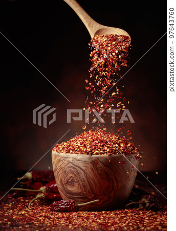 Chilli flakes are poured into a wooden dish. Chilli flakes are poured into a wooden dish. 97643760