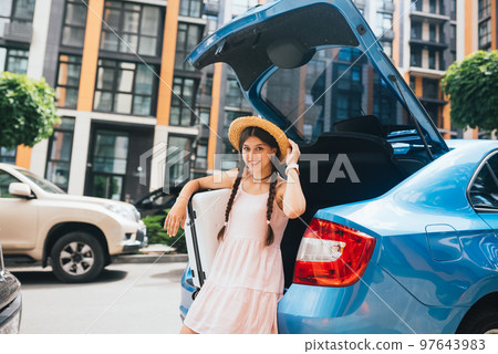 Woman packing her suitcase into luggage boot of the car. 97643983
