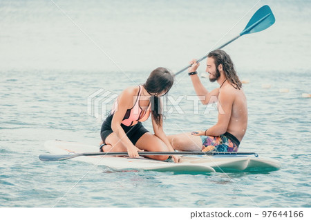 Sea woman and man on sup. Silhouette of happy young woman and man, surfing on SUP board, confident paddling through water surface. Idyllic sunset. Active lifestyle at sea or river. Sea woman and man on sup. Silhouette of happy young woman and man, surfing on SUP board, confident paddling through water surface. Idyllic sunset. Active lifestyle at sea or river. 97644166