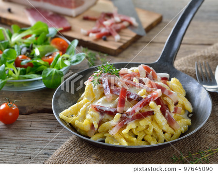 Hearty spaetzle with cheese sauce and South Tyrolean bacon served in an iron frying pan  97645090