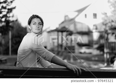 Girl enjoying city view from a bench in sunset or sunrise time. Beautiful blond-haired pretty girl in summer green park against sunset beams. Lonely woman sitting alone moments sunset. On Blurred Girl enjoying city view from a bench in sunset or sunrise time. Beautiful blond-haired pretty girl in summer green park against sunset beams. Lonely woman sitting alone moments sunset. On Blurred 97645321