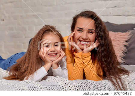 Love of young mother and daughter. They lie on the bed at home and have fun Love of young mother and daughter. They lie on the bed at home and have fun 97645487