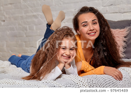 Love of young mother and daughter. They lie on the bed at home and have fun Love of young mother and daughter. They lie on the bed at home and have fun 97645489