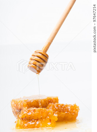 honey spoon through which fresh honey falls onto a honeycomb 97647254