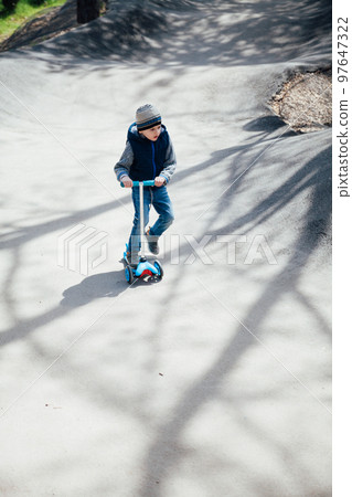 a little boy on a scooter rides through the streets of the city 97647322