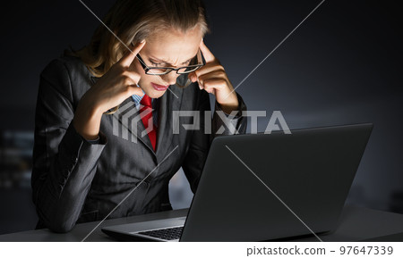 Tired businesswoman sitting at desk with laptop 97647339