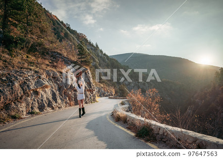 The woman is dear to the mountains. A woman in a white sweater, black boots and a hat walks along a winding alpine path between the mountains at the end of summer at sunset. Travel concept. 97647563