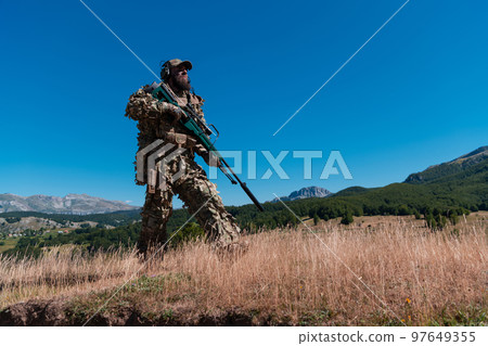 Army soldier holding a sniper rifle with scope and walking in the forest. war, army, technology and people concept. 97649355