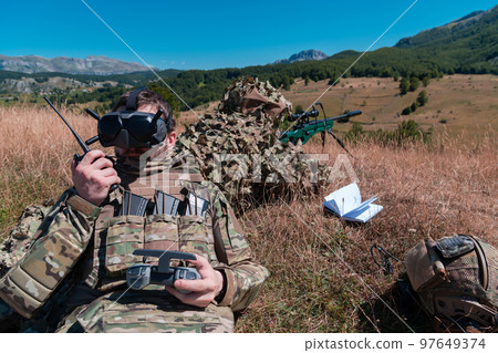 Sniper soldier assisted by an assistant to observe the area to be targeted with modern warfare tactical virtual reality goggles aerial drone military technology. Sniper soldier assisted by an assistant to observe the area to be targeted with modern warfare tactical virtual reality goggles aerial drone military technology. 97649374