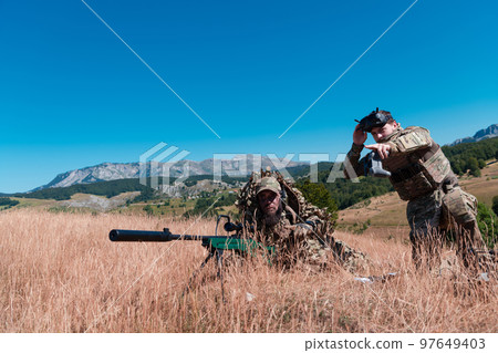 Sniper soldier assisted by an assistant to observe the area to be targeted with modern warfare tactical virtual reality goggles aerial drone military technology. 97649403