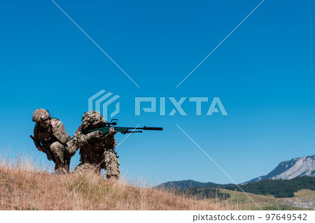A sniper team squad of soldiers is going undercover. Sniper assistant and team leader walking and aiming in nature with yellow grass and blue sky. Tactical camouflage uniform. A sniper team squad of soldiers is going undercover. Sniper assistant and team leader walking and aiming in nature with yellow grass and blue sky. Tactical camouflage uniform. 97649542