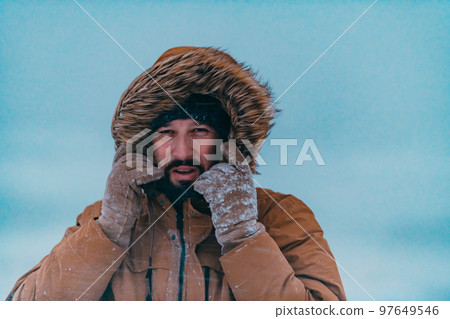 Headshot photo of a man in a cold snowy area wearing a thick brown winter jacket and gloves. Life in cold regions of the country. Headshot photo of a man in a cold snowy area wearing a thick brown winter jacket and gloves. Life in cold regions of the country. 97649546