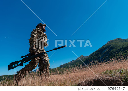 Army soldier holding a sniper rifle with scope and walking in the forest. war, army, technology and people concept. Army soldier holding a sniper rifle with scope and walking in the forest. war, army, technology and people concept. 97649547