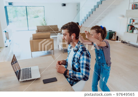 Work from home. Daughter interrupting her father while he is having a business online conversation on his laptop while sitting in modern living room Work from home. Daughter interrupting her father while he is having a business online conversation on his laptop while sitting in modern living room 97649565
