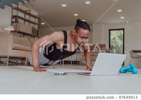Training At Home. Sporty man doing training while watching online tutorial on laptop, exercising in living room, free space Training At Home. Sporty man doing training while watching online tutorial on laptop, exercising in living room, free space 97649913