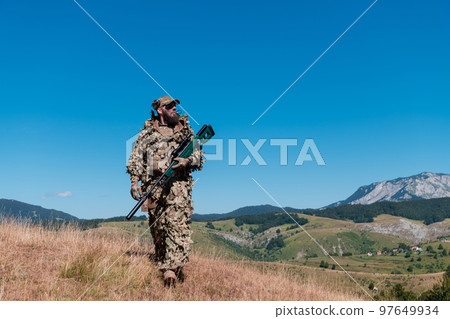 Army soldier holding a sniper rifle with scope and walking in the forest. war, army, technology and people concept. Army soldier holding a sniper rifle with scope and walking in the forest. war, army, technology and people concept. 97649934