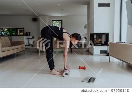 A young woman in sports clothes preparing sports equipment for online training in her living room A young woman in sports clothes preparing sports equipment for online training in her living room 97650148