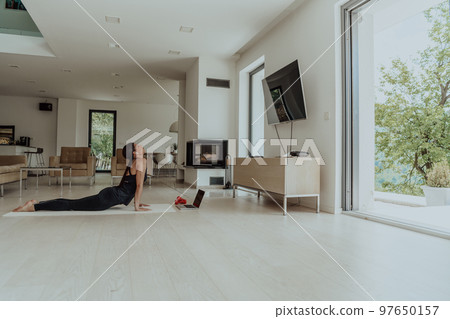 Young Beautiful Female Exercising, Stretching and Practising Yoga with Trainer via Video Call Conference in Bright Sunny House. Healthy Lifestyle, Wellbeing and Mindfulness Concept. 97650157