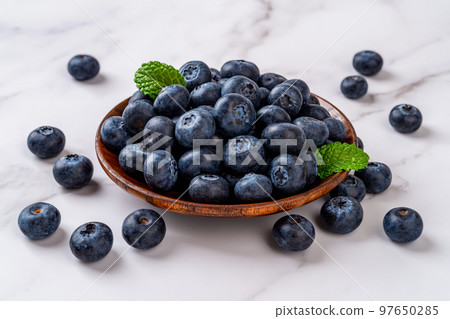 Ripe blueberry on a wooden plate over marble background.  97650285